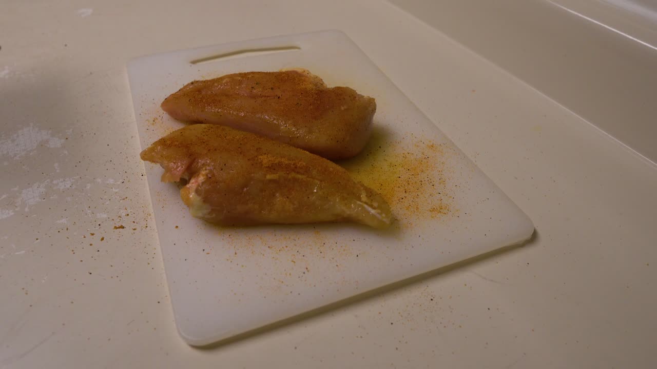 Raw Chicken that has be seasoned is now being peppered with an automatic pepper grinder