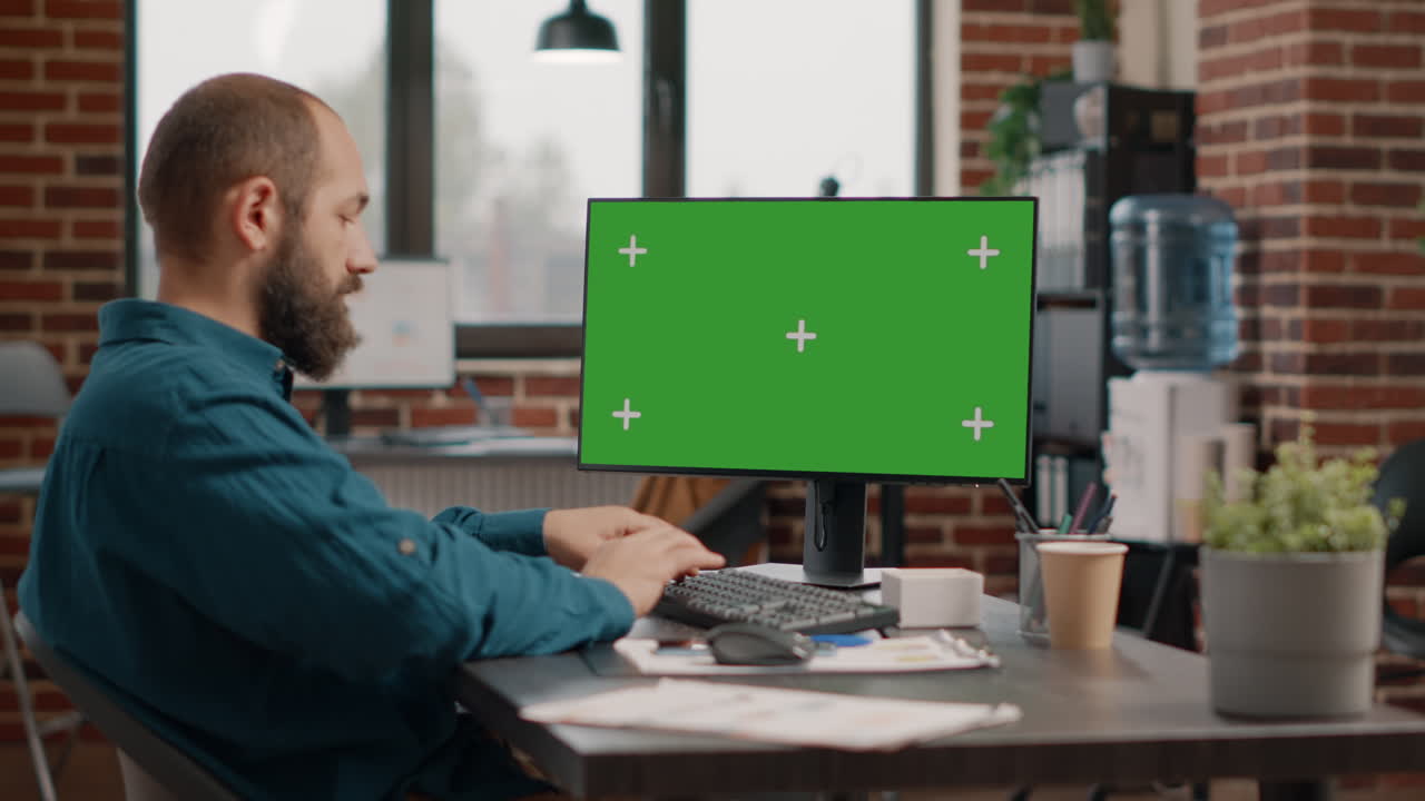 Man working on computer with green screen in office