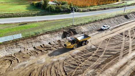 drone footage captures an excavator and dump truck at a construction site in cromwell, new zealand, under bright daylight
