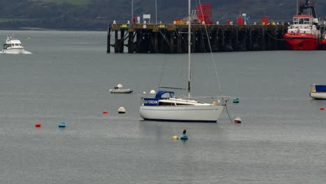 wide-Shot-of-sail-yacht-with-docks-in-background-with-power-boat-passing-through-frame