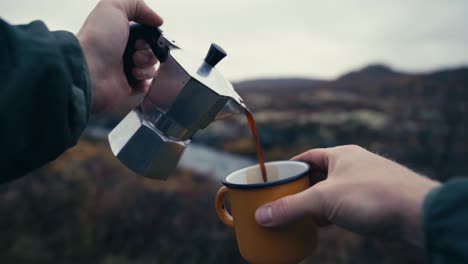 man hands pouring coffee into travel mug from coffee pot with nature landscape