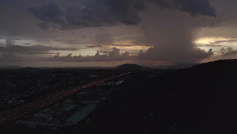 disparo aéreo volando hacia atrás de una carretera que conduce a una colina con nubes pesadas en el horizonte