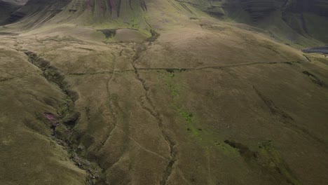 Brecon-beacons-countryside-green-cracked-valley-birdseye-Llyn-y-fan-Fach-aerial-view-tilt-up-to-ragged-majestic-mountain-peak