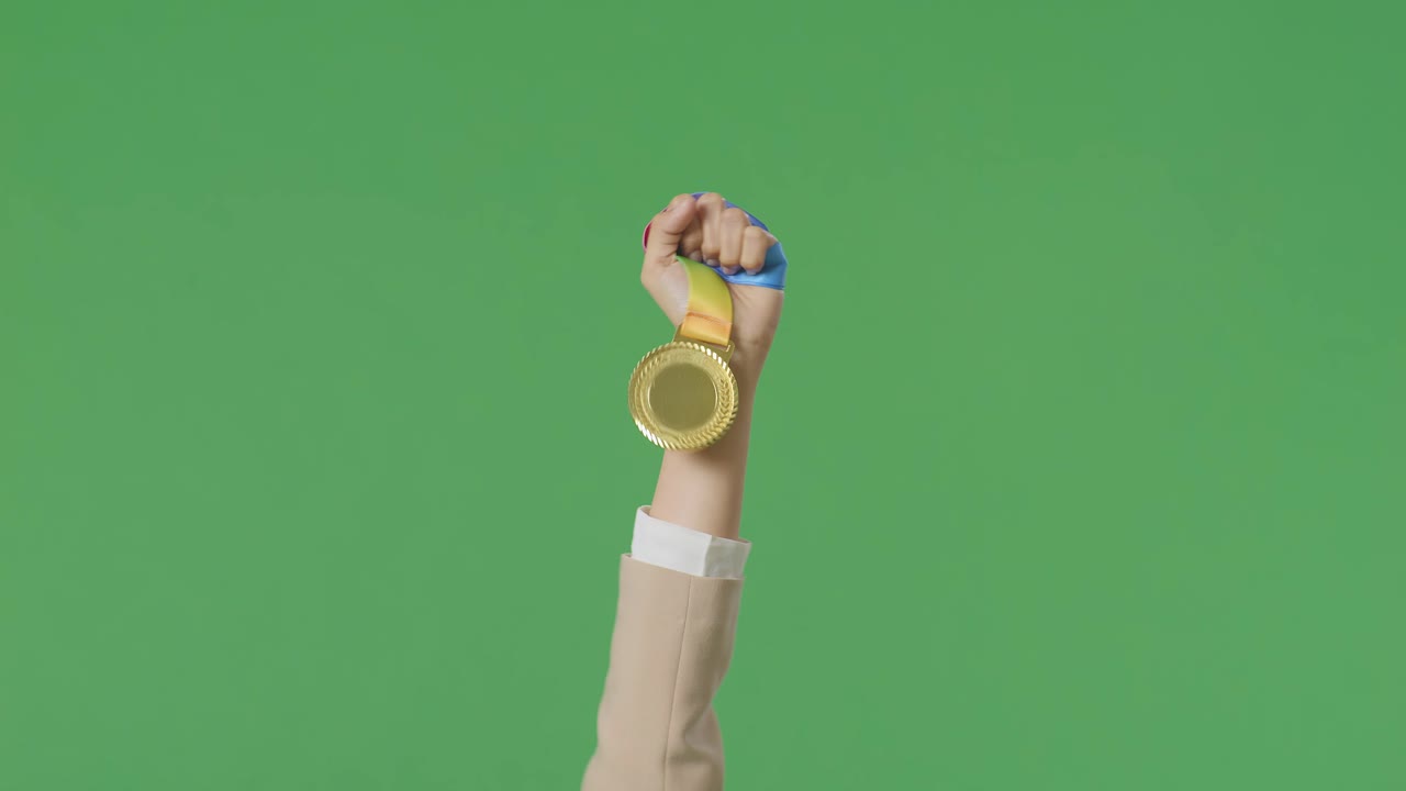 스튜디오의 녹색 화면 배경에서 첫 번째 우승자로 우승을 축하하기 위해 공중에 금메달을 들고 있는 사업가의 손