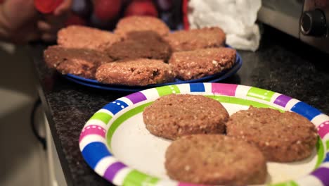 seasoning plant based burger patties on a blue plate and a multi coloured paper plate for a summertime barbecue cookout, shot in 60 frames per second 4k