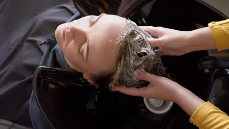 hands of caucasian female hairdresser washing hair of relaxed female customer at hair salon