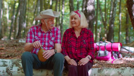 tired thirsty senior hikers grandmother grandfather with backpacks relaxing drinking water in wood