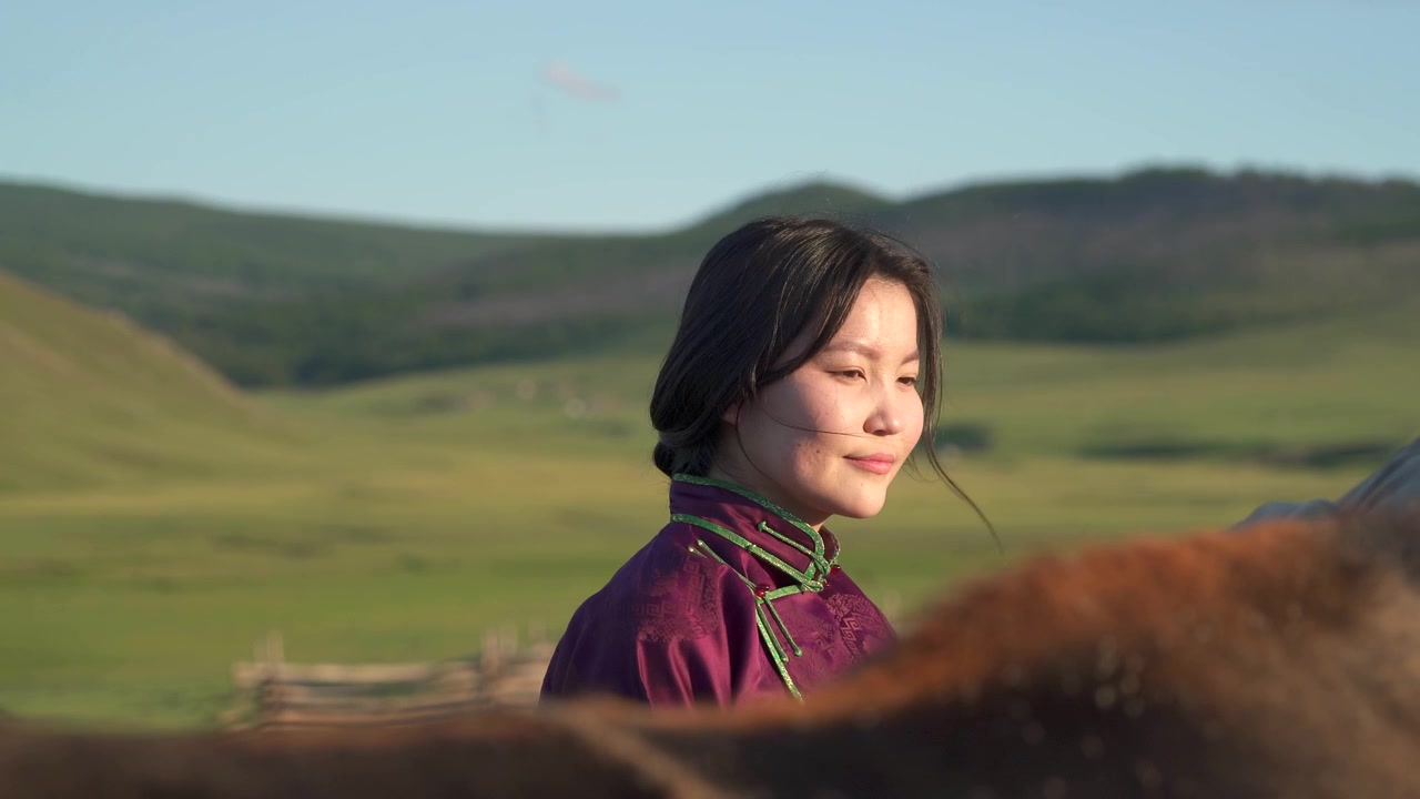 Ung mongolsk kvinde i traditionel beklædning står udendørs med hest