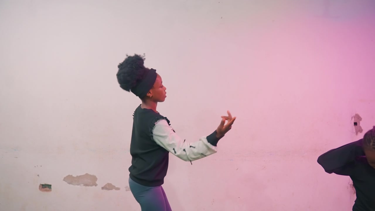Black mother and child dancing against pink wall, playful rehearsal and training, spontaneous jumps and steps, laughter and rhythm, active movement practice, casual studio setting, joyful connection