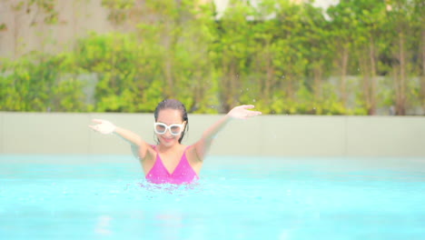 Fröhliche-Exotische-Frau-Mit-Nassen-Haaren-Spielt-Mit-Wasser-Im-Swimmingpool-Des-Luxuriösen-Tropischen-Resorts,-Zeitlupe