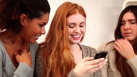 cute female friends using smartphone while sitting on couch