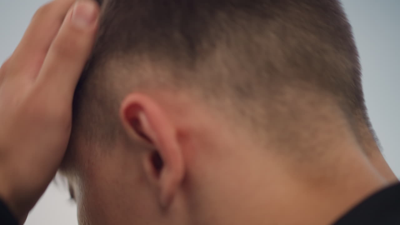 코카서스 남성이 손으로 두피와 귀를 만지면서 짧은 페이드컷을 정리하는 클로즈업 장면, 행사 전 불안한 듯 치장하는 모습, 부드러운 흐린 하늘, 도시 옥상 배경, 머리카락과 손가락의 섬세한 질감