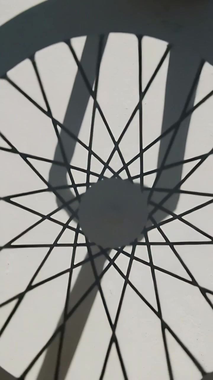 Video verticale: Ruota di bicicletta che gira creando ombre mutevoli dei raggi su una parete chiara al sole, ombra della forcella.
