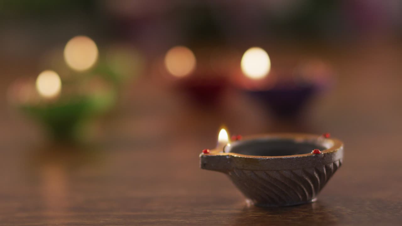 Candele accese in vasetti decorativi di terracotta su un tavolo di legno, fuoco su quello in primo piano, sfondo bokeh