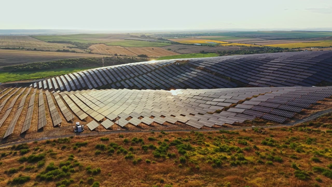 Solpaneler dækker et stort landområde i landlige omgivelser på en solskinsdag, hvor sollyset reflekteres fra overfladerne.