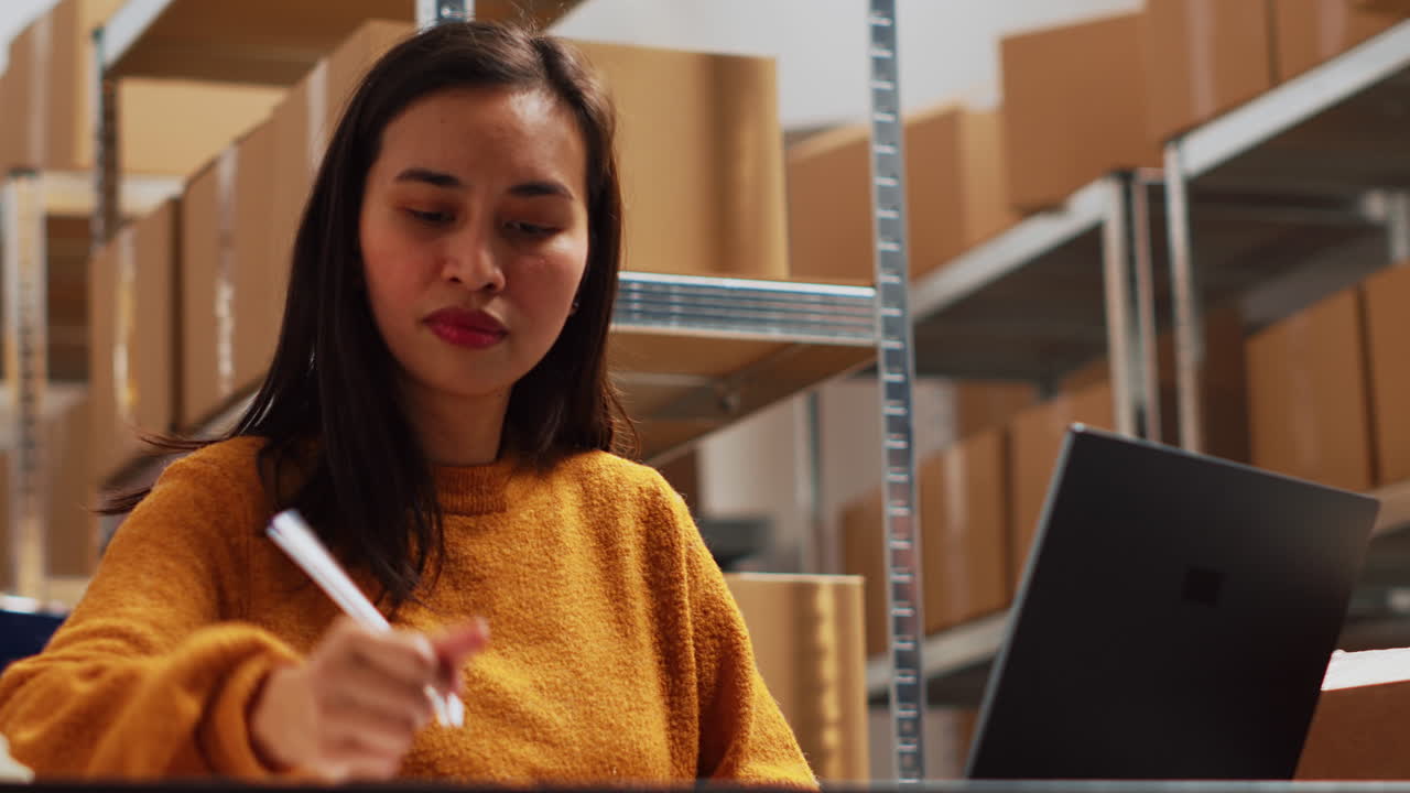 Woman working on laptop in warehouse with boxes