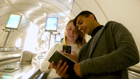 couple using technology on escalator in subway station