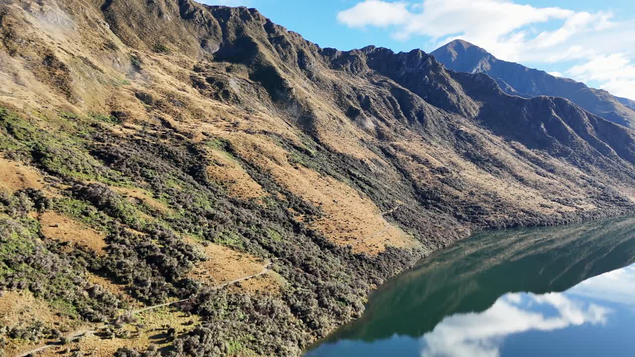 Aerial footage captures the serene landscape of Lake Moke with surrounding mountains under clear blue skies in Queenstown, New Zealand