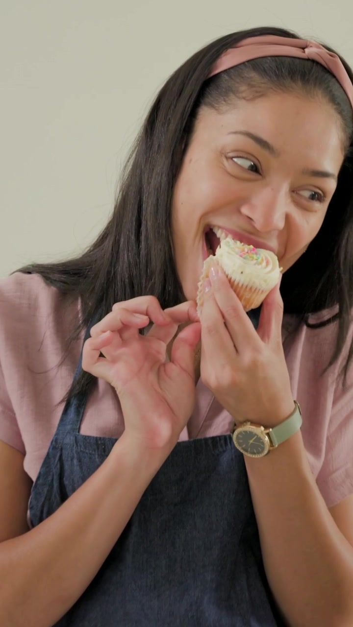 Vídeo vertical: Padeiro de avental estendendo a mão, testando cobertura de cupcake no balcão, trocando com criança.