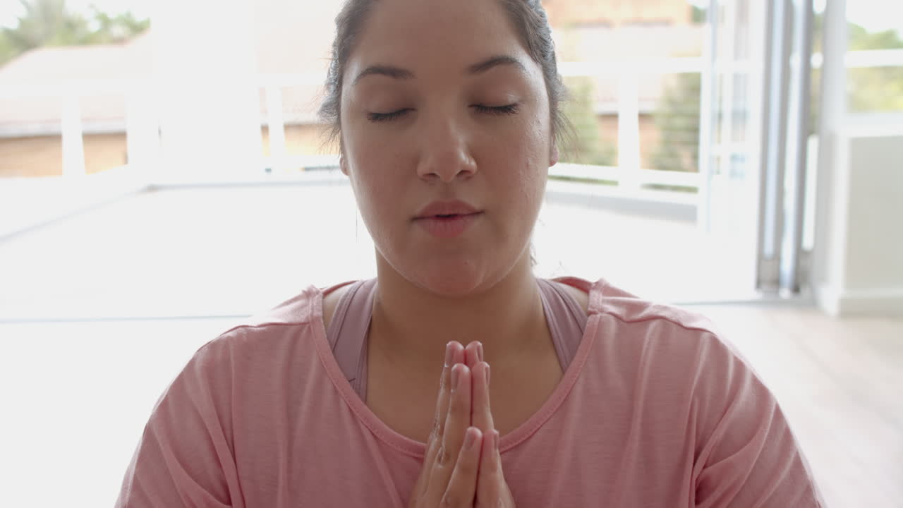 Donna birazziale curvy seduta sul pavimento che pratica yoga, meditazione e respirazione profonda, al rallentatore.