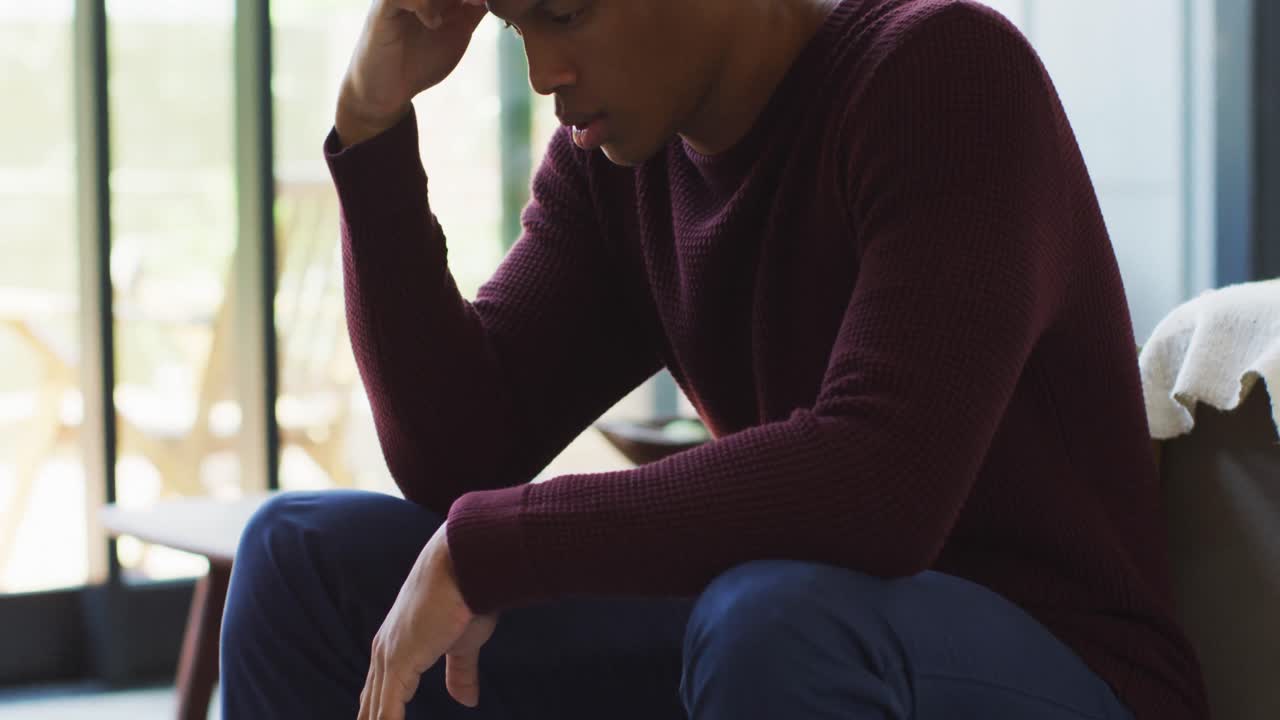 un hombre afroamericano preocupado está sentado en casa solo.