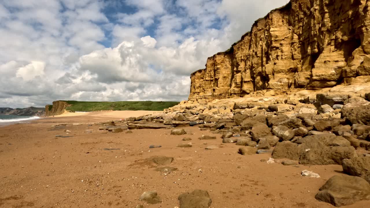 Wide angle shot of a coastline cliff on a Jurassic Coast beach. Stablised footage moves from right to left with the cliffs on the right of the frame, distant cliffs, beach in the foreground.