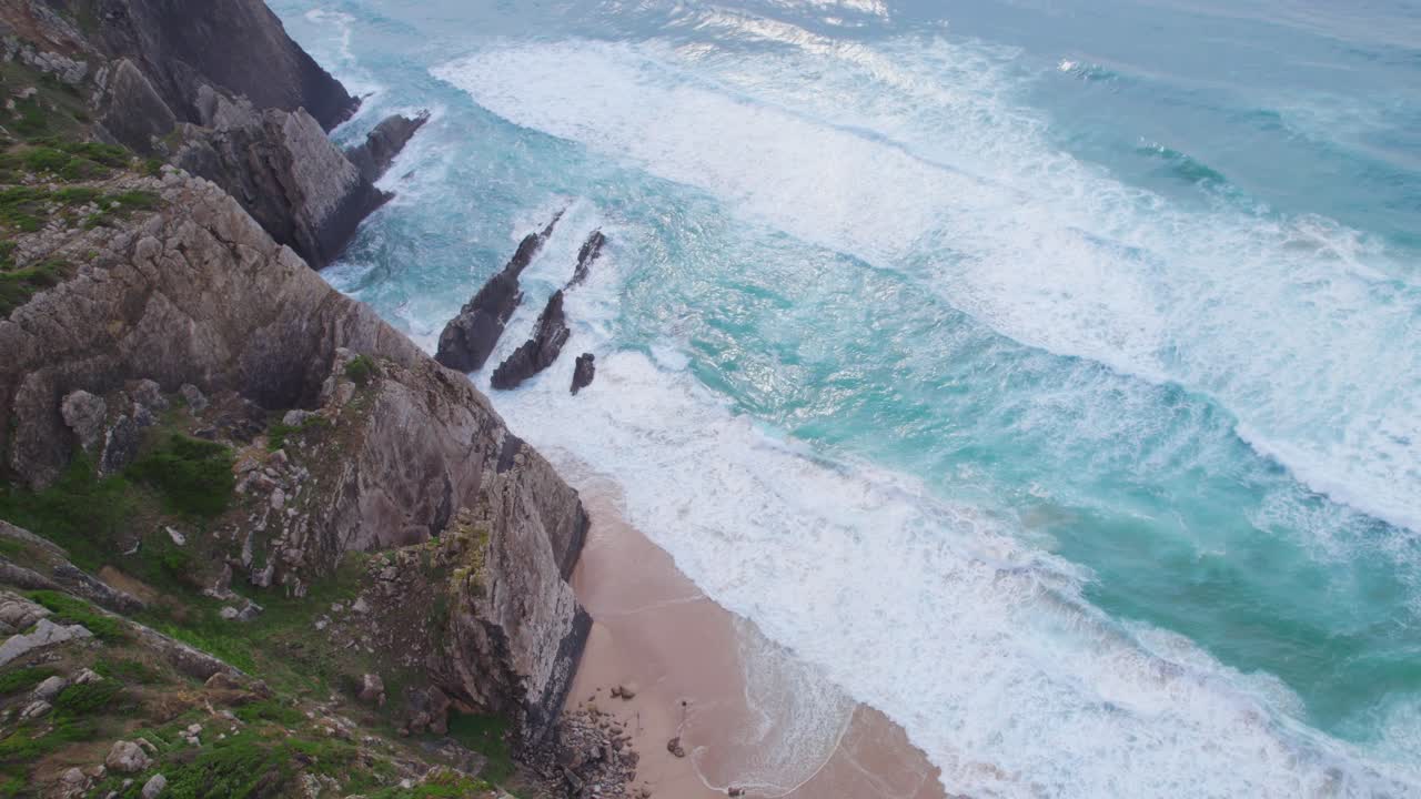 Praia da Ursa, Portugal – dramatic coastal scene where steep cliffs descend to a narrow beach with crashing waves and jagged rock formations jutting into the Atlantic Ocean