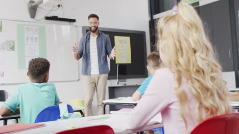 Diverse-male-teacher-and-schoolchildren-sitting-at-desks-in-classroom