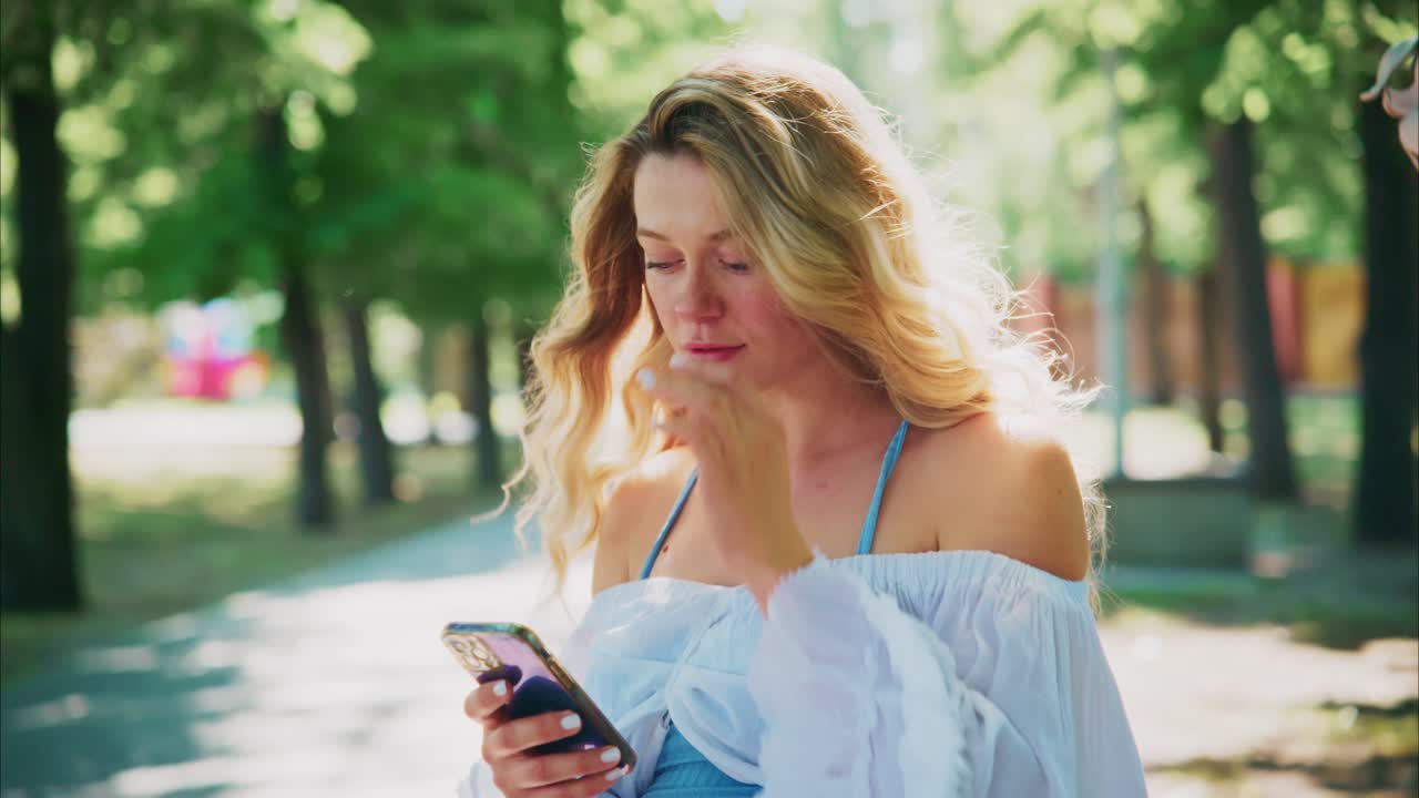 Giovane donna bionda che usa lo smartphone in un parco soleggiato