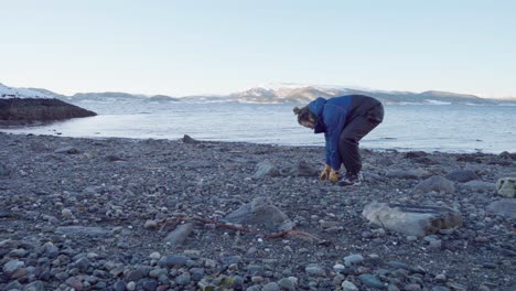 man picking up rocks by the river during his camping trip in indre fosen, norway