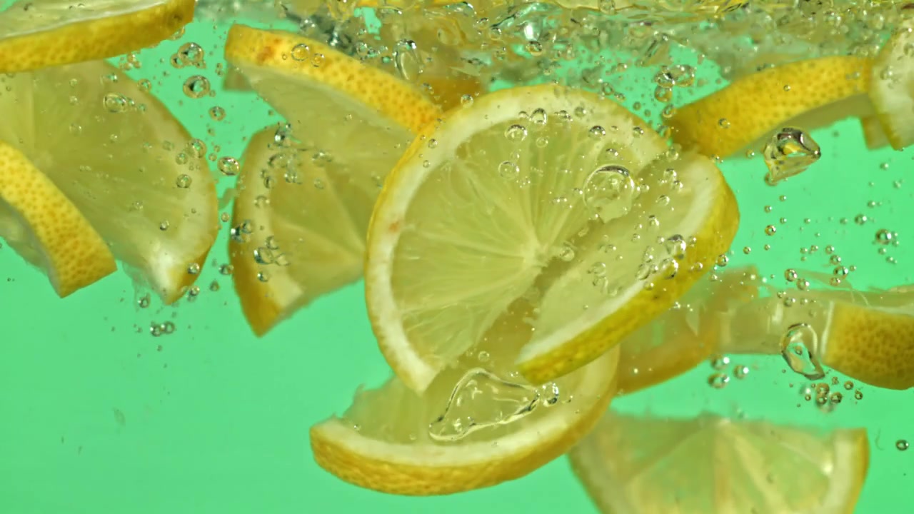 Fette di limone fresche che cadono in acqua con bolle su sfondo verde