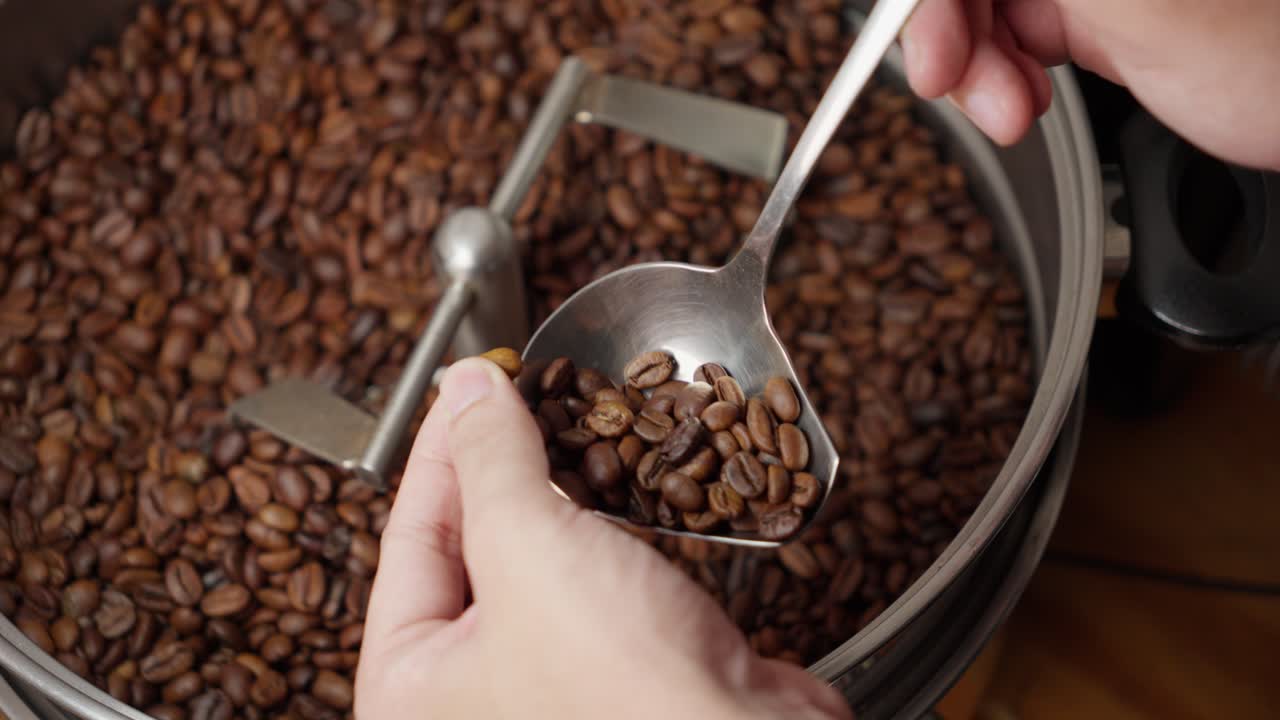 Coffee grinder blender closeup being mixed and tested with spoon, caucasian hand black grains