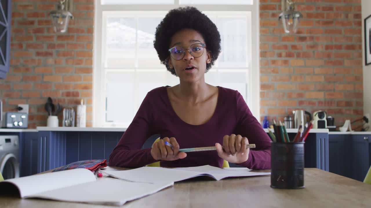 Happy african american teenage girl at kitchen table in online lesson using laptop computer