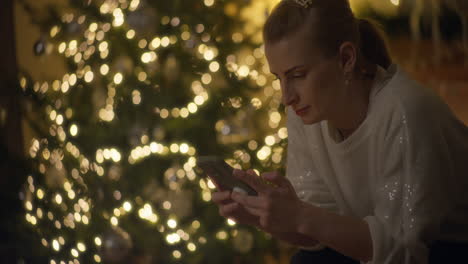 mujer usando el teléfono cerca del árbol de navidad