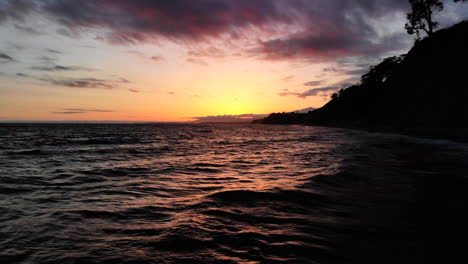 flying low over the ocean waves with colorful sunset reflections on the beach in santa barbara, california aerial drone