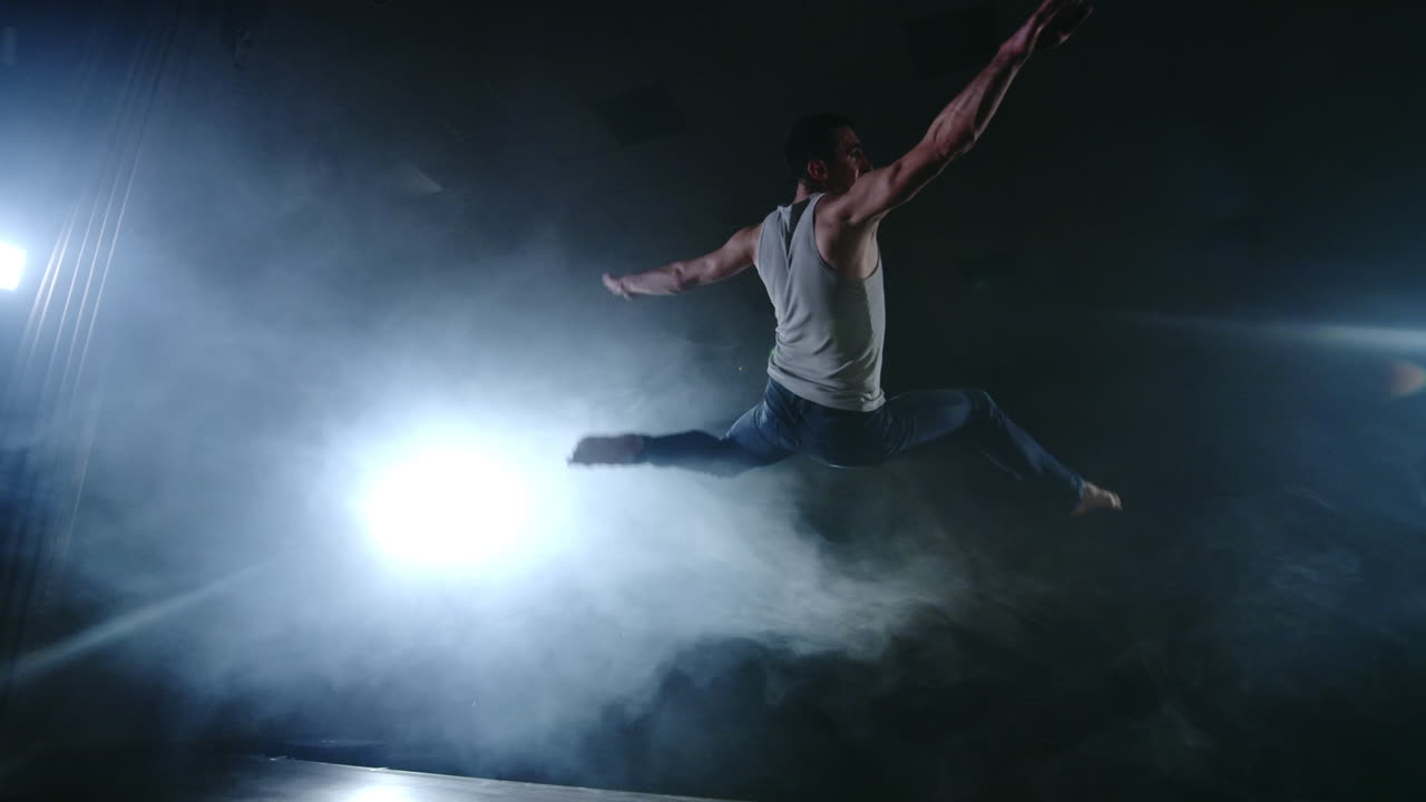 un ballet moderno un hombre realiza saltos y giros a la luz de los reflectores y el humo en un fondo oscuro. ensayo de coreografía acrobática del guión del ballet moderno.