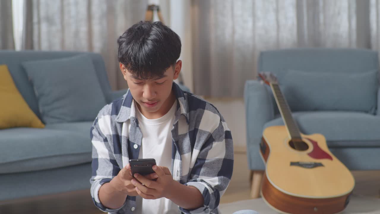 아시아 십대 부부, 집에 오는 소녀는 스마트폰으로 바닥에 앉아있는 남자친구를 놀라게합니다.