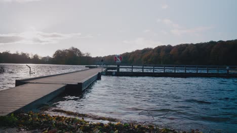 Tall-Scandinavian-Man-With-Cap-Stands-Up-and-Walks-Down-The-Bridge-on-Gyllebo-Lake-in-Österlen-Sweden---Static-Wide-Shot