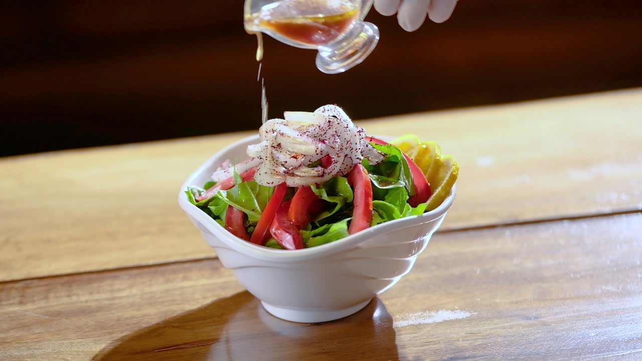 Kitchen chef pours oil on salad plate in slow motion