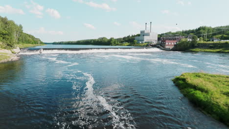 low aerial shot flies over river with hydroelectric dam and power plant in the background, maine usa