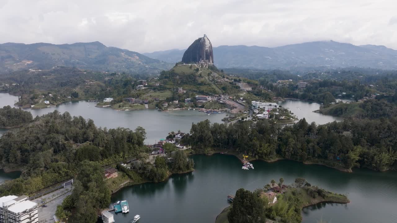 Drone shot retreating El Peñón de Guatapé (La Piedra Rock) with lakes and mountains on a cloudy day