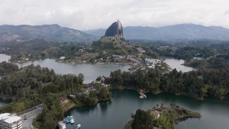 Drone shot retreating El Peñón de Guatapé (La Piedra Rock) with lakes and mountains on a cloudy day