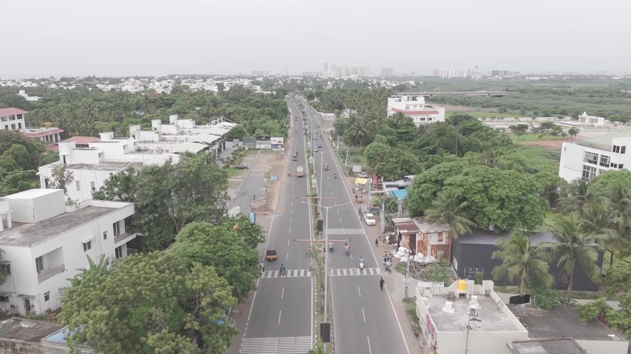 Il traffico scorre lungo un viale fiancheggiato da palme mentre un drone vola basso sopra le case di Chennai.