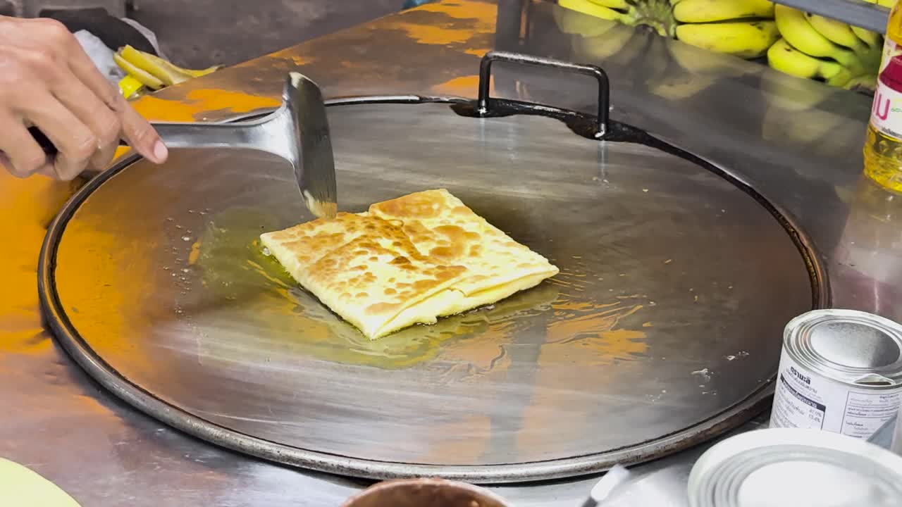 un vendedor callejero prepara hábilmente roti tailandés en una parrilla caliente en phuket, mostrando técnicas de cocina tradicionales y una vibrante cultura de comida callejera