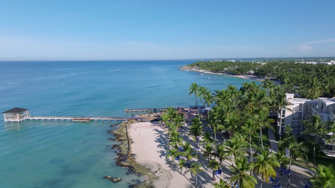 Aerial of a waterfront dock, crystal-clear waters, and white sandy beach at Dominicus Beach, Dominican Republic. Dolly in drone view