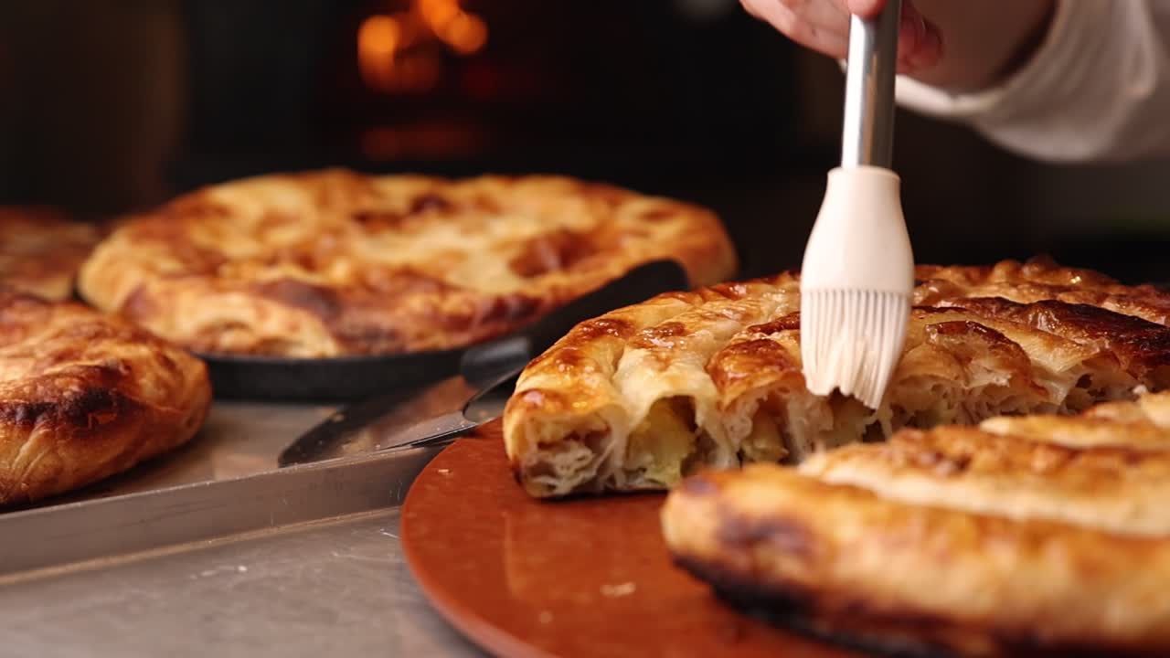 Mano che spennella con olio un prodotto da forno dorato in una cucina con forno tradizionale