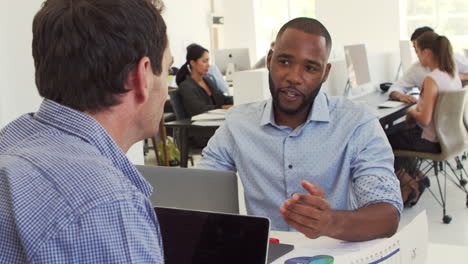 two men discussing business in a busy office