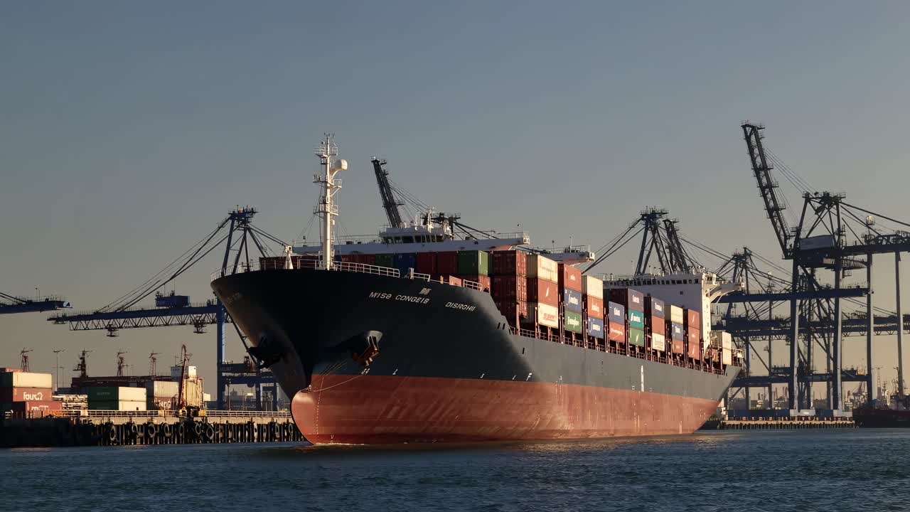 Wide-angle shot of a cargo ship docked at a bustling port, showcasing industrial cranes