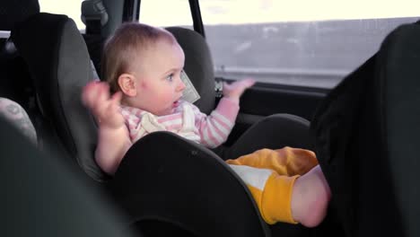 niña pequeña sentada en el asiento de bebé mientras el coche está conduciendo. bebé viajando en un asiento de coche en la parte trasera del vehículo. viaje largo en coche. niño pequeño jugando, bebiendo. turismo y viajes, concepto de viaje.