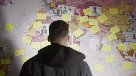 young man making notes on paper stickers stuck to investigation map and searching connections